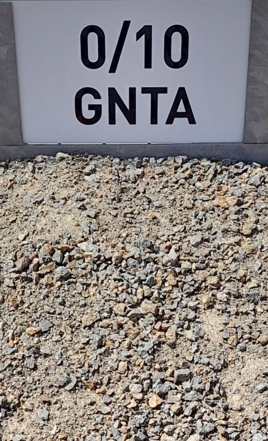 Tas de gravier fin de granulométrie 0/10, identifié par un panneau blanc avec l'inscription "0/10 GNTA" en lettres noires en arrière-plan.