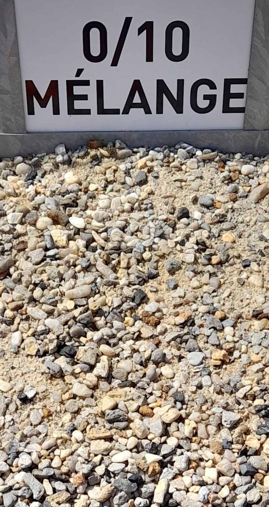 Tas de gravier varié, allant de sable fin à petits cailloux, avec une pancarte en arrière-plan indiquant "0/10 Mélange".