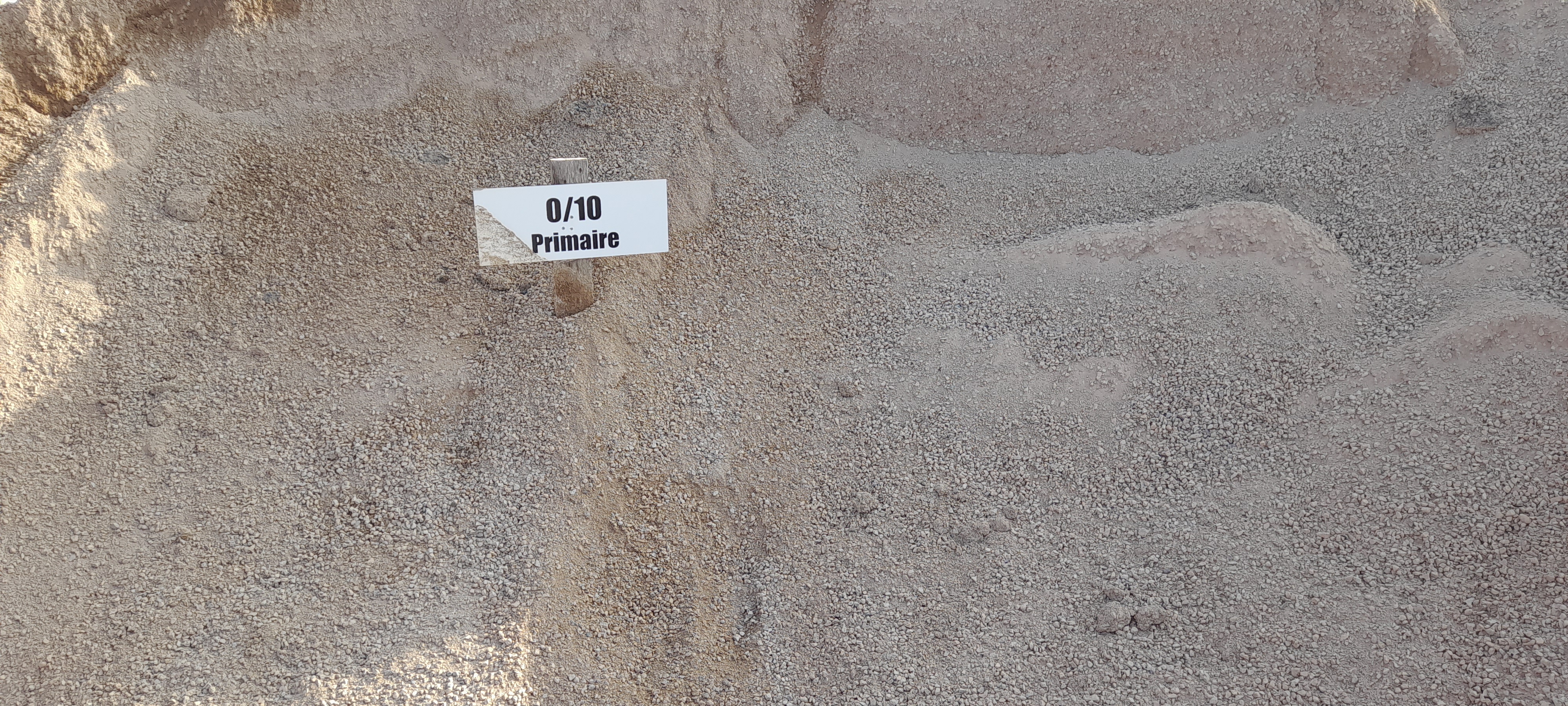 Vue rapprochée d'une section de sol sableux stratifié avec une étiquette blanche indiquant "0m". L'étiquette est placée au centre-gauche, marquant un repère de mesure. Les différentes couches de sable sont visibles avec des variations subtiles de teinte.
