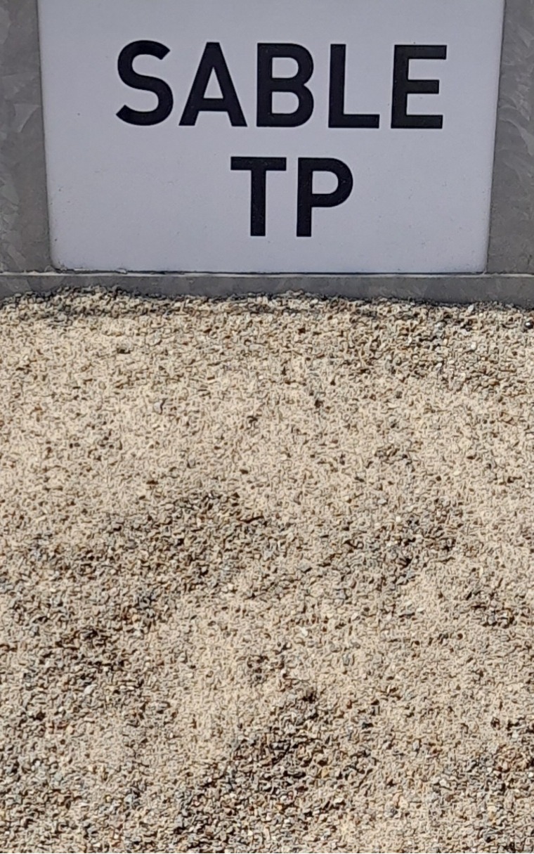 Tas de sable TP de couleur beige avec un panneau indiquant "SABLE TP" en lettres noires sur fond blanc, placé en arrière-plan.
