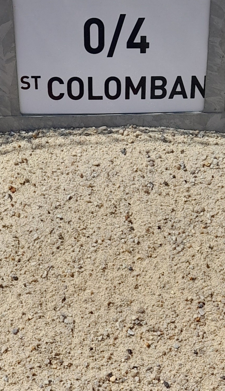 Vue rapprochée de sable fin beige, légèrement granuleux, avec un panneau blanc en arrière-plan indiquant "0/4 St Colomban" en lettres noires majuscules.