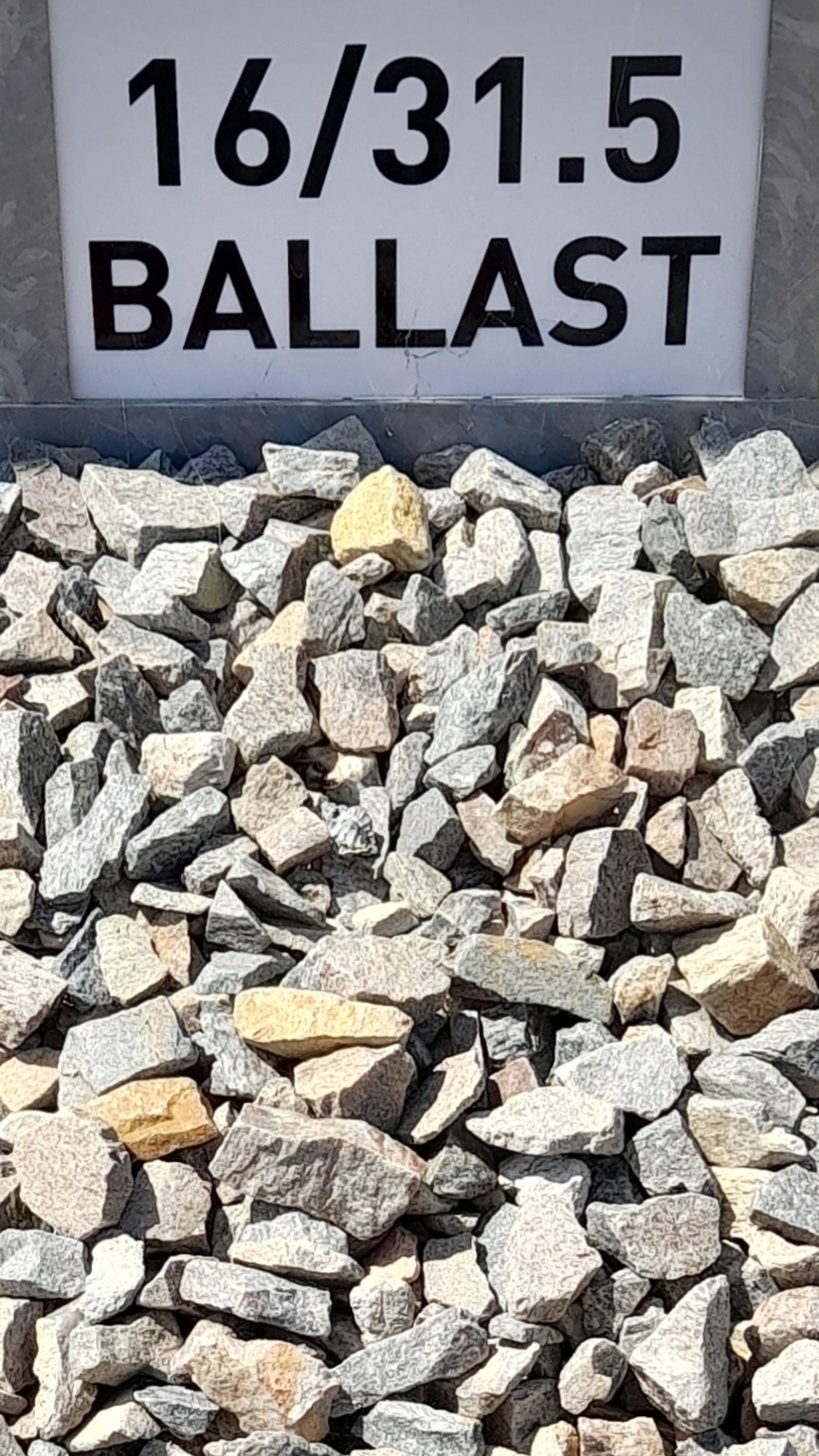 Tas de ballast de granulométrie 16/31.5 mm, composé de pierres grises et beige clair, affiché sous un panneau blanc marqué "16/31.5 BALLAST" en lettres noires.