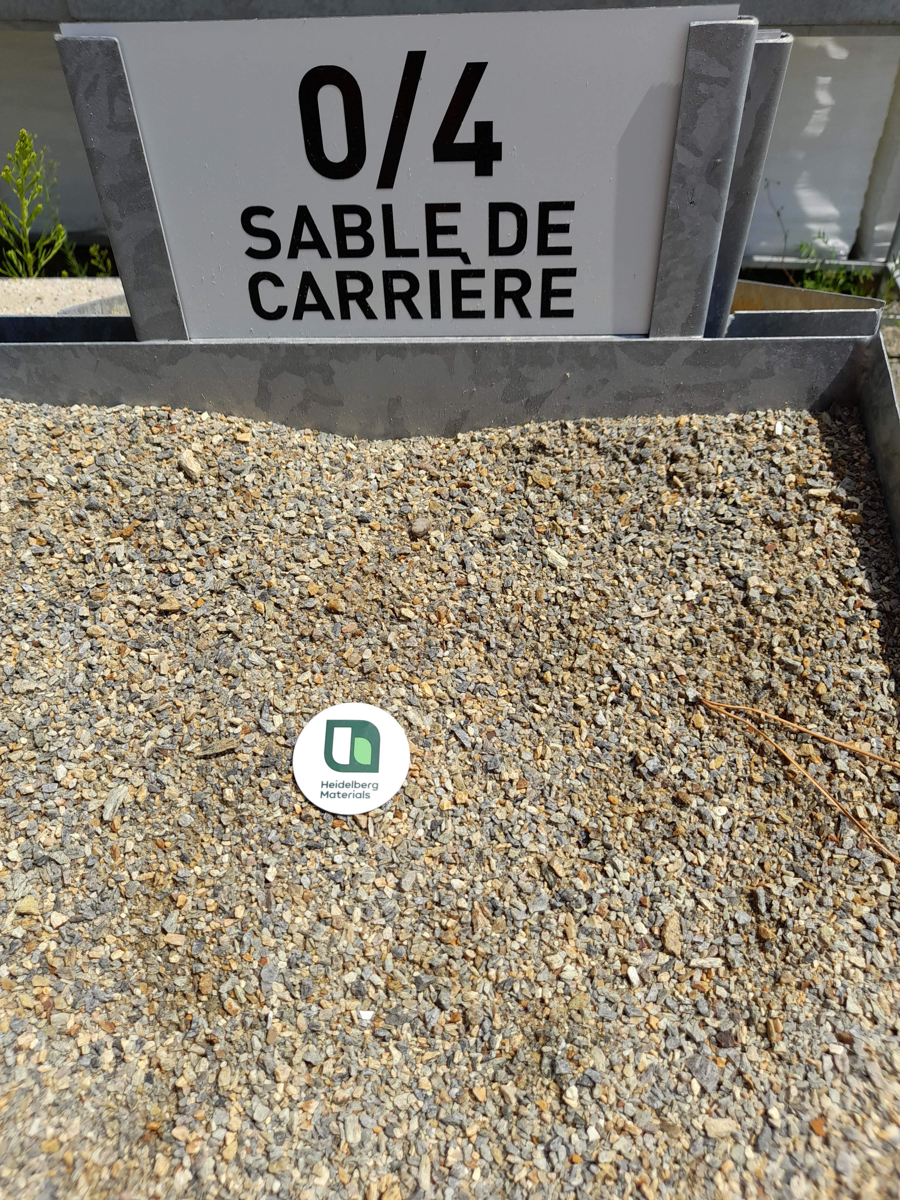 Tas de sable de carrière granulométrie 0/4, avec un panneau indiquant "0/4 Sable de Carrière" en haut et un disque vert marqué d’un logo au centre du sable.