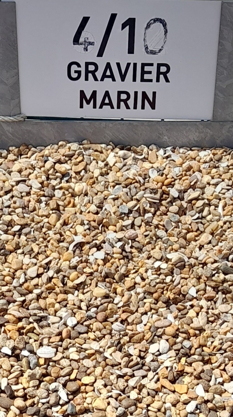 Tas de gravier marin de calibre 4/10, composé de petits cailloux aux teintes beige, blanc et jaune, exposé dans un bac métallique avec une étiquette indiquant "4/10 GRAVIER MARIN" en haut.