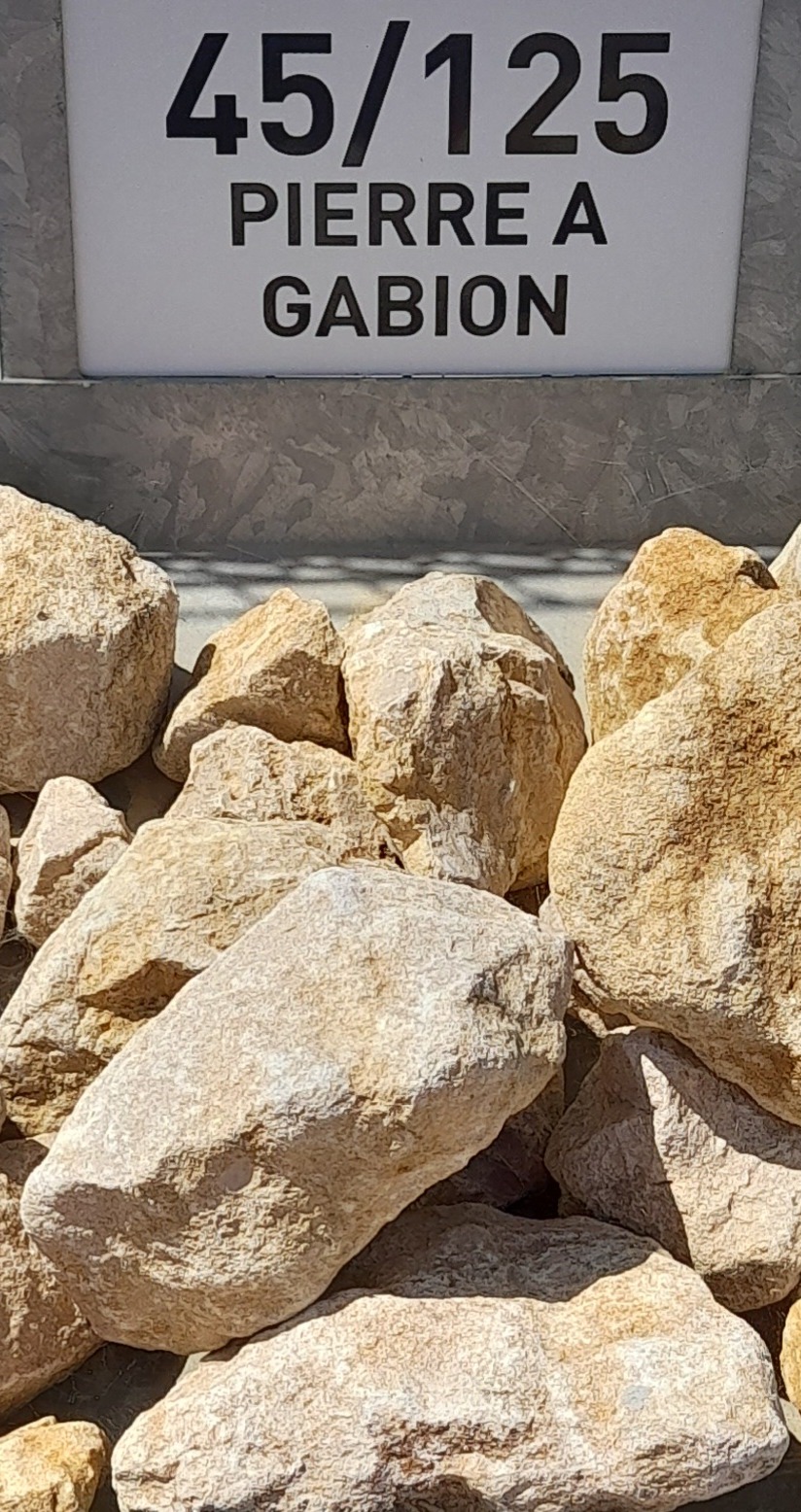 Tas de pierres à gabion beige clair avec un panneau indiquant "45/125 PIERRE A GABION" en arrière-plan.