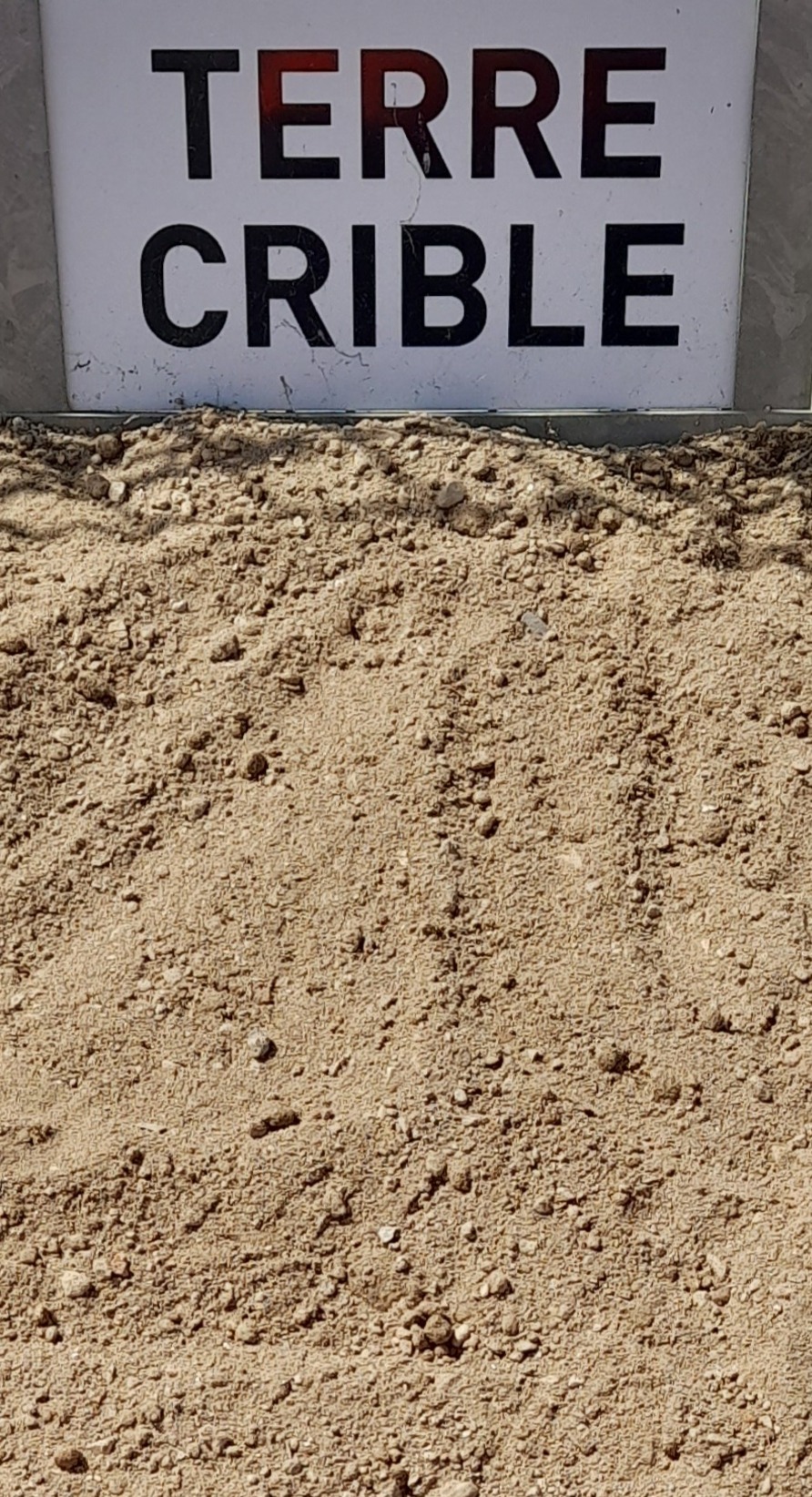Panneau blanc portant l'inscription "TERRE CRIBLÉE" en haut, avec un tas de terre tamisée beige visible en dessous, montrant une texture fine et homogène.